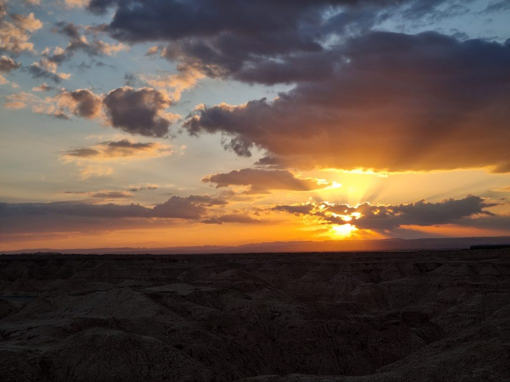 שקיעה במדבר עם קרני שמש החודרות דרך עננים מעל גבעות בערבה